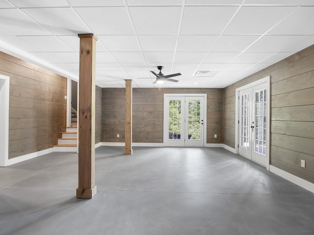 below grade area with french doors, wood walls, baseboards, stairs, and a ceiling fan