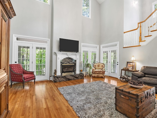 living area with a towering ceiling, a stone fireplace, light wood finished floors, and healthy amount of natural light