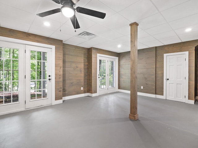unfurnished room with finished concrete floors, baseboards, wooden walls, healthy amount of natural light, and a paneled ceiling