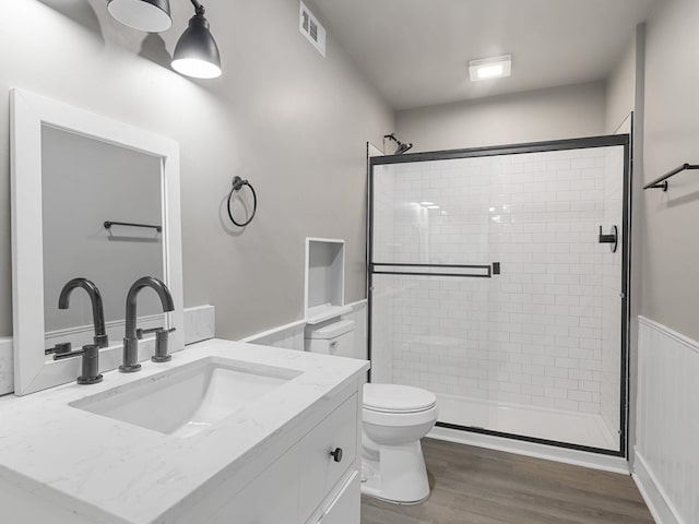 bathroom with a shower stall, wood finished floors, toilet, a wainscoted wall, and vanity