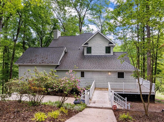rear view of property with roof with shingles, a chimney, and a deck