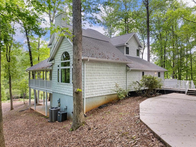 view of side of home with a patio, a shingled roof, a deck, and a chimney