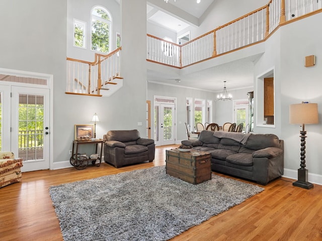 living room featuring a towering ceiling, a chandelier, plenty of natural light, wood finished floors, and ornamental molding