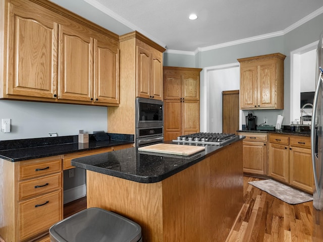 kitchen with a kitchen island, appliances with stainless steel finishes, wood finished floors, ornamental molding, and dark stone countertops