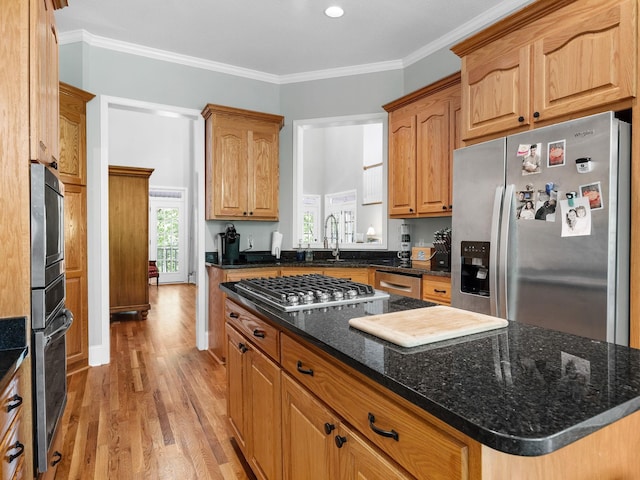 kitchen with stainless steel appliances, light wood finished floors, a kitchen island, dark stone counters, and crown molding