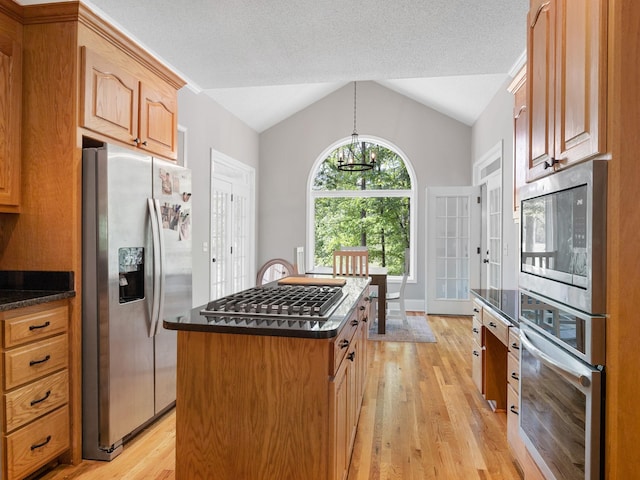 kitchen featuring stainless steel appliances, light wood-style floors, dark countertops, lofted ceiling, and a kitchen island