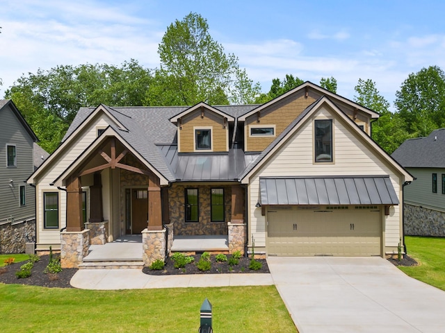 view of front facade with a standing seam roof, covered porch, concrete driveway, stone siding, and a front yard