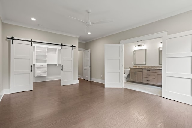 unfurnished bedroom with a barn door, a sink, crown molding, wood finished floors, and recessed lighting