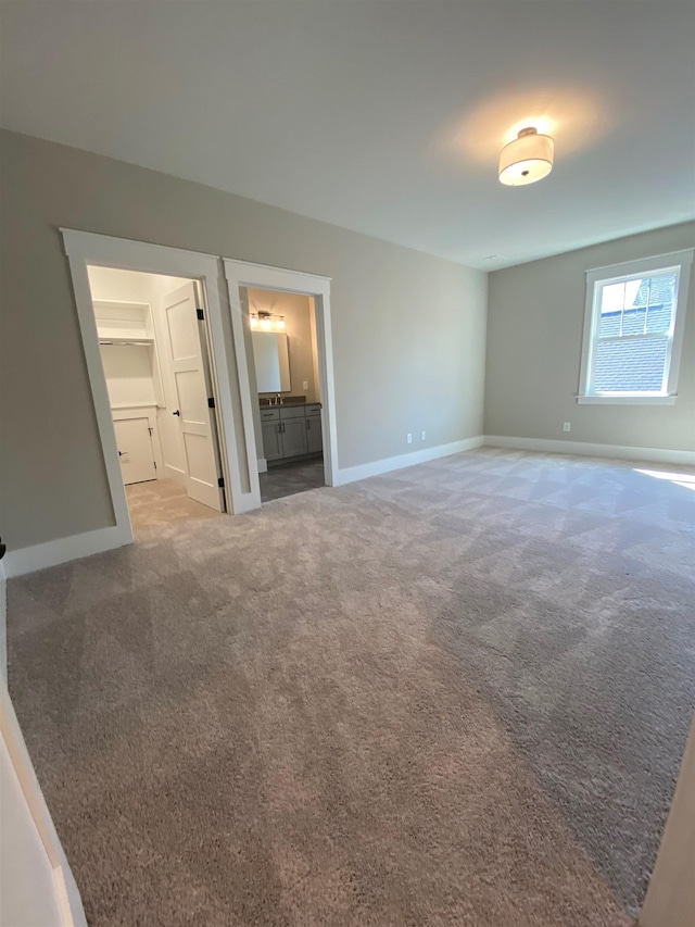 unfurnished bedroom featuring baseboards, carpet flooring, a walk in closet, and ensuite bath