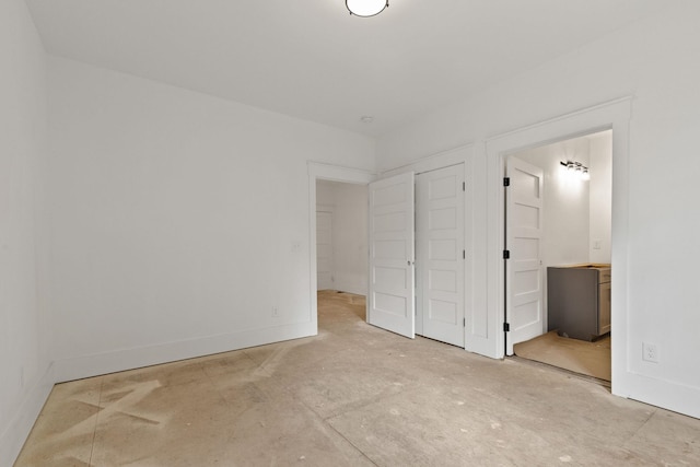 unfurnished bedroom featuring baseboards, ensuite bathroom, and concrete floors