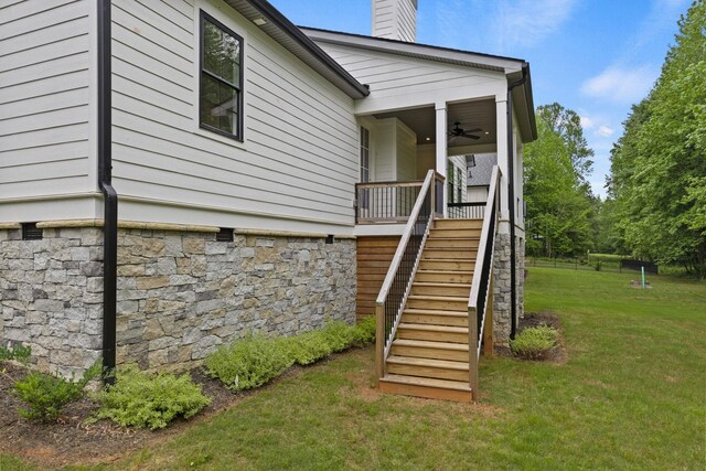 doorway to property with ceiling fan, a yard, a chimney, and stone siding