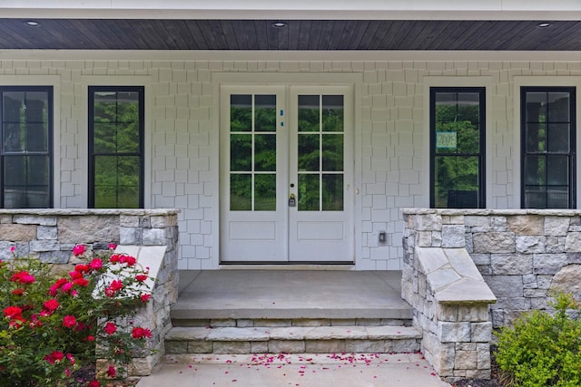 doorway to property featuring a porch, french doors, and stone siding