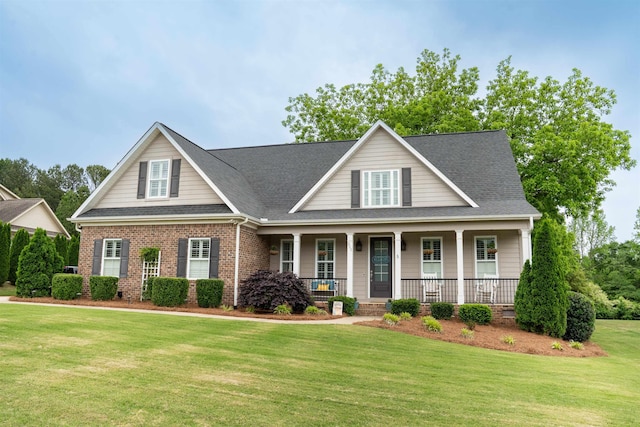 view of front of home featuring a front yard, roof with shingles, a porch, and brick siding