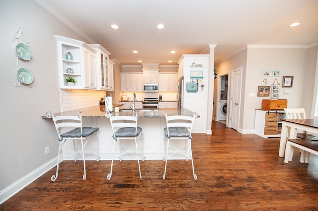 kitchen with washer / dryer, appliances with stainless steel finishes, a peninsula, backsplash, and light stone counters