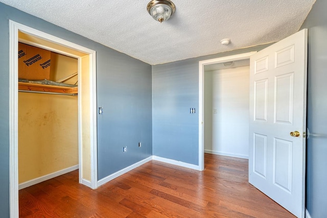 unfurnished bedroom featuring wood finished floors, a textured ceiling, baseboards, and a closet