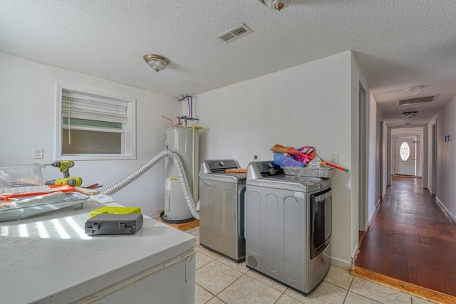 laundry room featuring water heater, separate washer and dryer, light tile patterned floors, and a textured ceiling