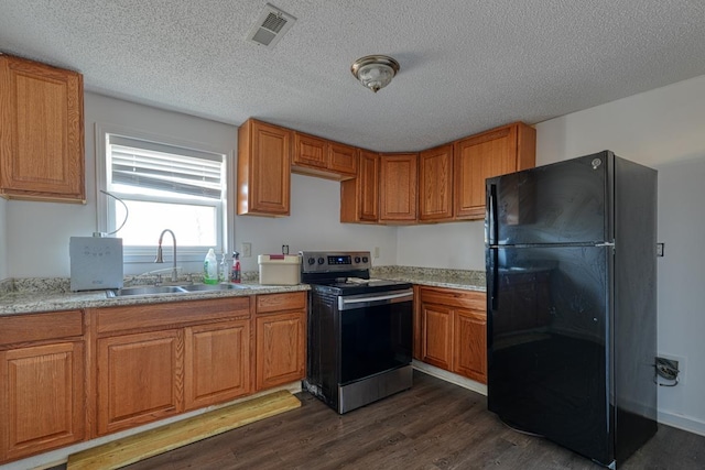 kitchen with freestanding refrigerator, stainless steel electric stove, a sink, brown cabinetry, and dark wood finished floors
