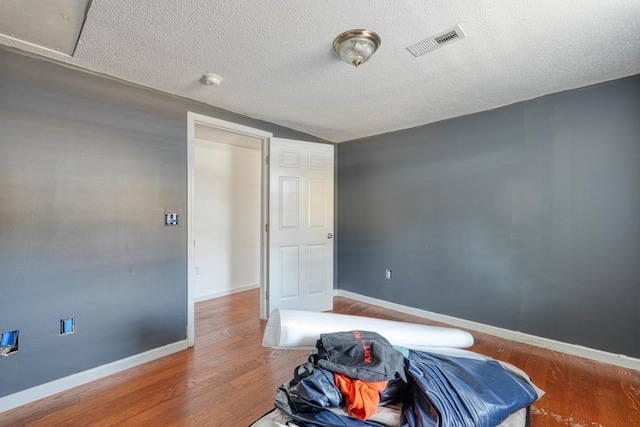bedroom with wood finished floors, a textured ceiling, and baseboards