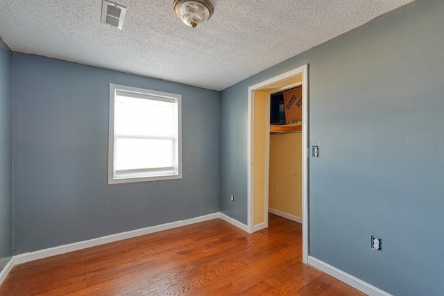 unfurnished bedroom featuring wood finished floors, a closet, baseboards, a textured ceiling, and a walk in closet