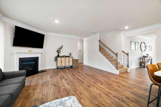 living area with crown molding, stairs, hardwood / wood-style floors, a fireplace with flush hearth, and recessed lighting