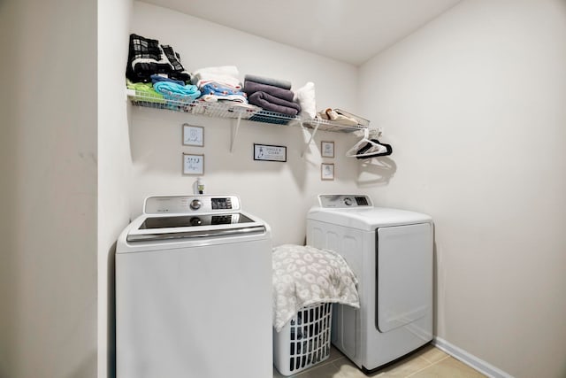 clothes washing area with washer and clothes dryer, light tile patterned flooring, and baseboards