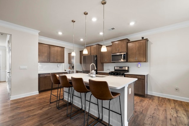 kitchen featuring appliances with stainless steel finishes, a sink, a kitchen island with sink, decorative backsplash, and a kitchen bar