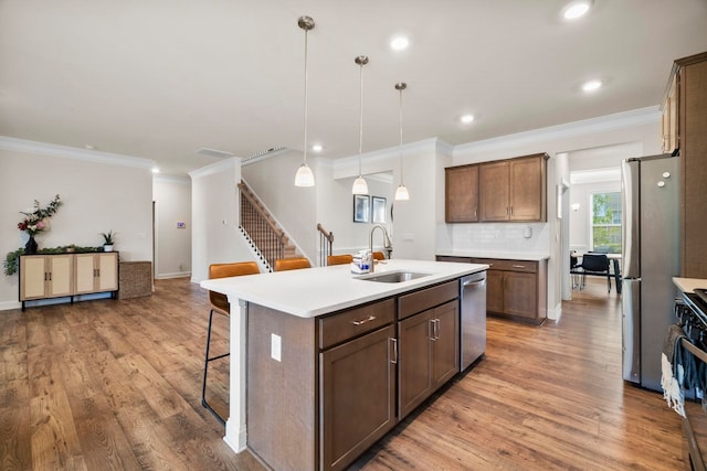 kitchen with a sink, stainless steel appliances, a breakfast bar area, crown molding, and light wood finished floors