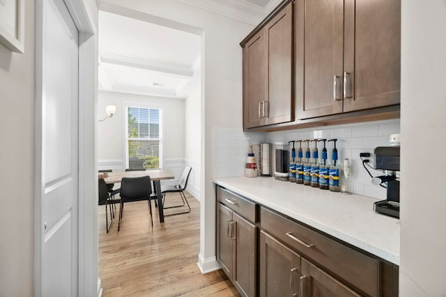 bar featuring light wood-style floors, tasteful backsplash, crown molding, wainscoting, and a raised ceiling