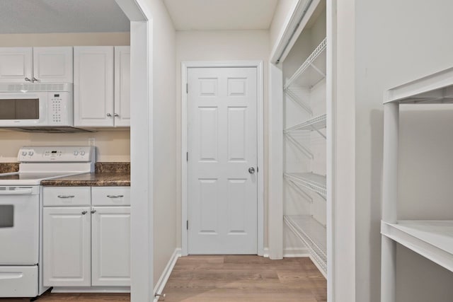kitchen with white appliances, white cabinets, light wood-type flooring, and dark countertops
