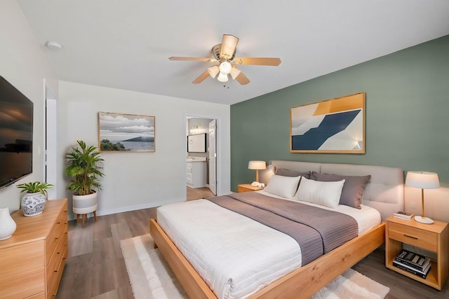 bedroom featuring wood finished floors, ensuite bath, a ceiling fan, and baseboards