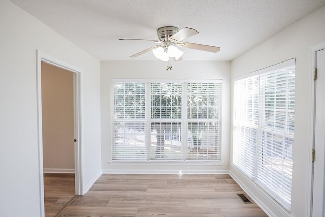 empty room featuring a ceiling fan, plenty of natural light, light wood-type flooring, and a textured ceiling