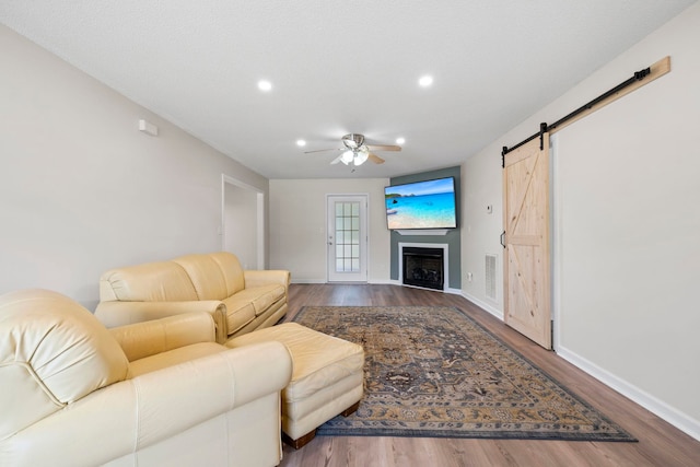 living room with ceiling fan, wood finished floors, a barn door, recessed lighting, and baseboards