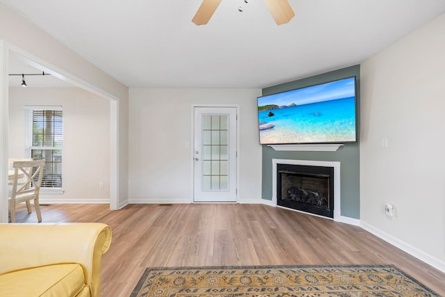 unfurnished living room with light wood-style floors, ceiling fan, baseboards, and a glass covered fireplace