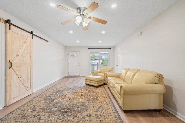 living room with a barn door, light wood-style floors, a ceiling fan, baseboards, and recessed lighting