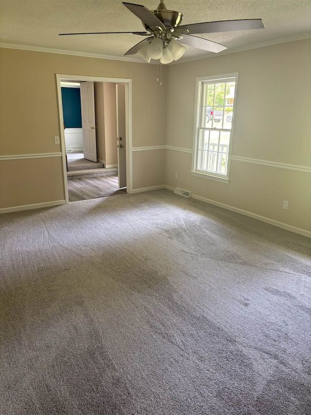 carpeted empty room featuring a textured ceiling, a ceiling fan, ornamental molding, and baseboards