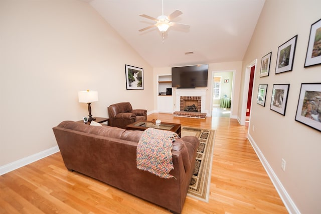 living room with light wood-type flooring, a ceiling fan, baseboards, a brick fireplace, and high vaulted ceiling