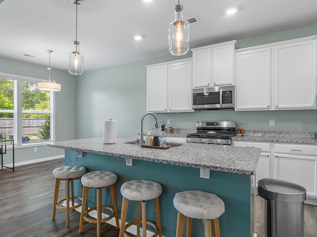 kitchen with stainless steel appliances, dark wood finished floors, a sink, white cabinets, and a kitchen island with sink