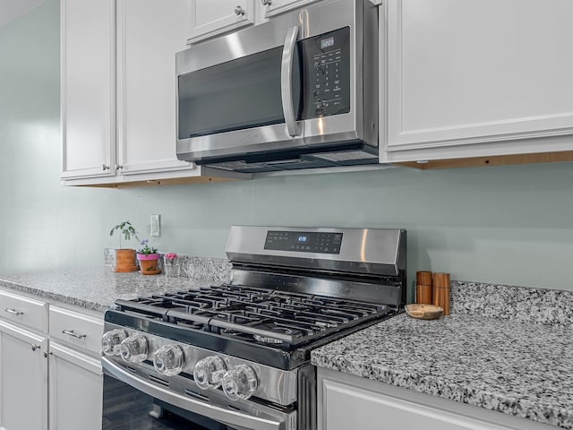 kitchen with stainless steel appliances, white cabinetry, and light stone counters