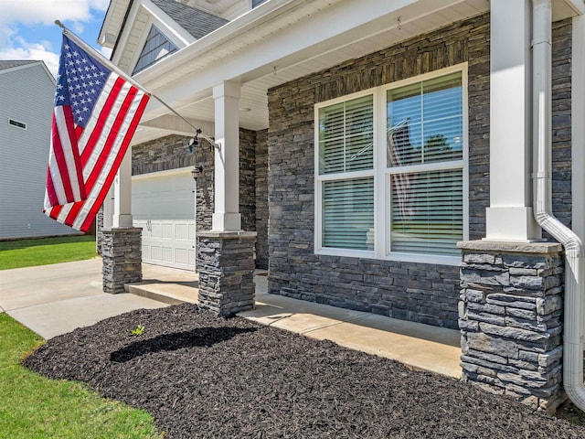 property entrance featuring a porch, stone siding, a garage, and concrete driveway