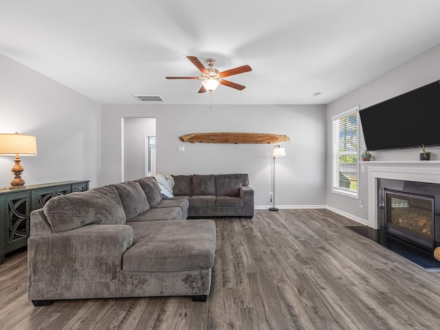 living area with wood finished floors, a ceiling fan, a fireplace with flush hearth, and baseboards