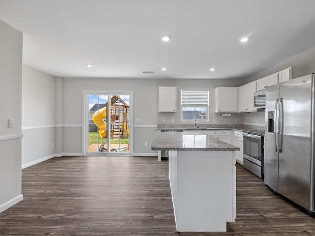 kitchen featuring appliances with stainless steel finishes, a kitchen island, white cabinetry, light stone countertops, and dark wood-style floors