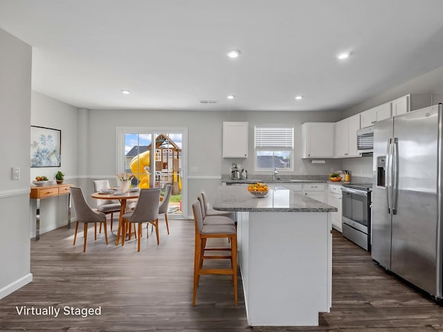 kitchen featuring appliances with stainless steel finishes, a center island, white cabinets, light stone counters, and dark wood-style floors