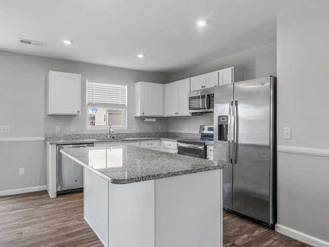 kitchen with appliances with stainless steel finishes, white cabinetry, a sink, a kitchen island, and dark wood-style flooring