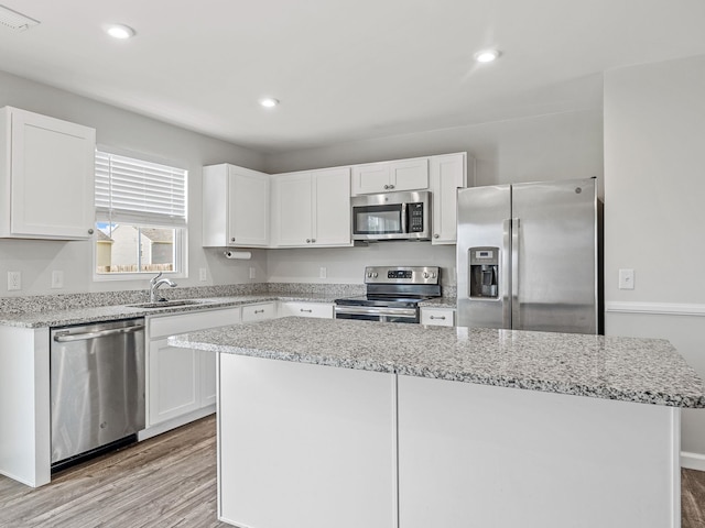 kitchen with stainless steel appliances, a sink, light wood-style flooring, a kitchen island, and white cabinetry