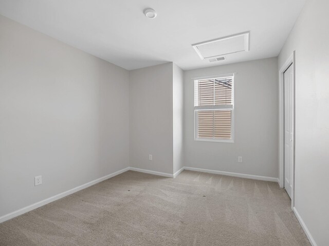 empty room featuring attic access, light carpet, and baseboards