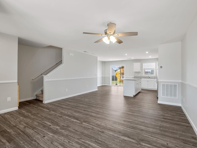 unfurnished living room featuring a ceiling fan, dark wood-type flooring, baseboards, recessed lighting, and stairway