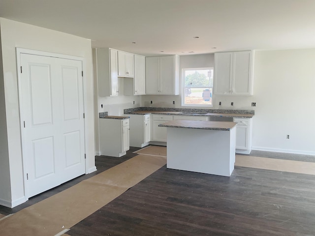 kitchen featuring dark wood-style floors, a center island, baseboards, and white cabinets