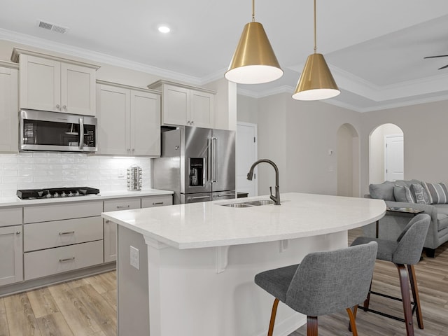 kitchen with appliances with stainless steel finishes, a sink, arched walkways, light wood-style floors, and a breakfast bar area