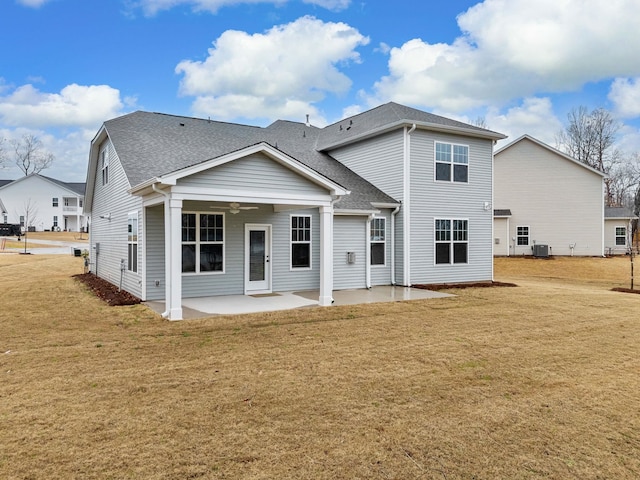 back of property with ceiling fan, a patio, roof with shingles, and a lawn