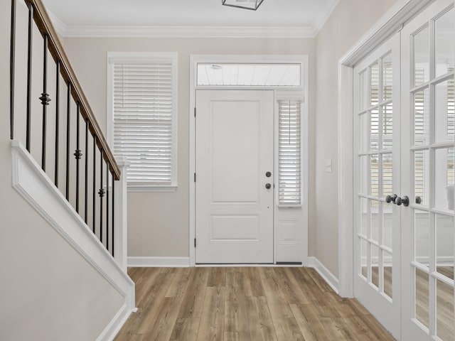 foyer featuring light wood finished floors, ornamental molding, baseboards, plenty of natural light, and french doors